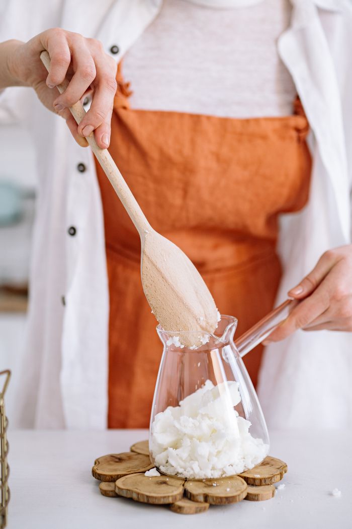 Home Close-up of a woman crafting candles with soy wax, mixing ingredients indoors with wooden tools.